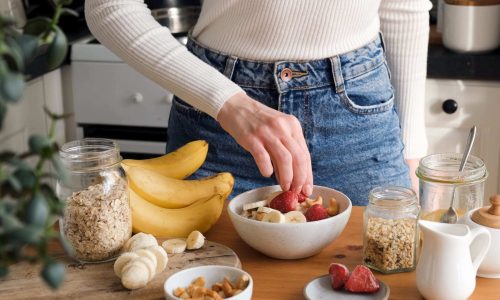 Adding fruits to breakfast oatmeal porridge bowl. Woman preparing healthy breakfast at the kitchen. Concept of healthy eating and lifestyle