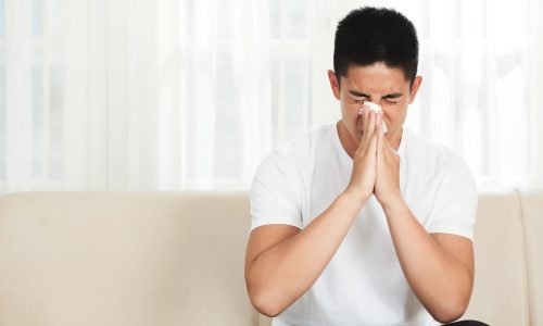 Young mixed-race man using paper tissue to blow his nose